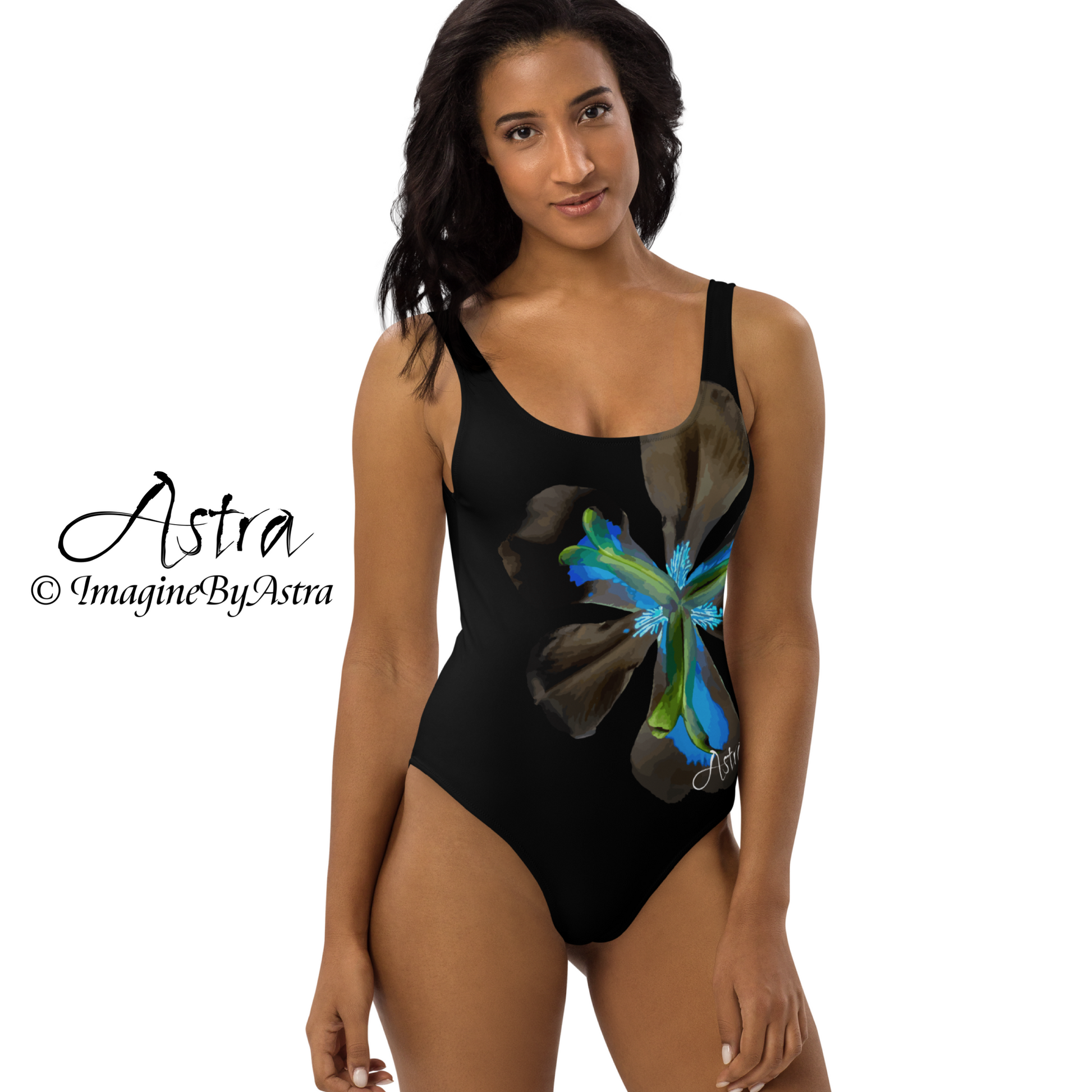 From the Astra Swimwear lineup: a black woman wears a black one-piece swimsuit with a large vibrant blue tropical flower graphic down the front. The swimsuit has a flattering high cut at the hips. Part of the Tropical Iris Collection by designer, Imagine By Astra.