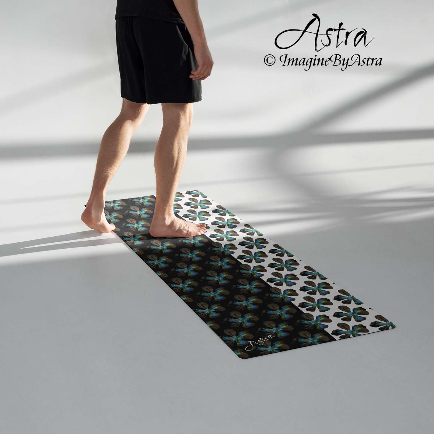 A person stands atop a yoga mat with a dramatic two toned black and white surface with a bright blue tropical flower print on top. From brand, Imagine by Astra Activewear.