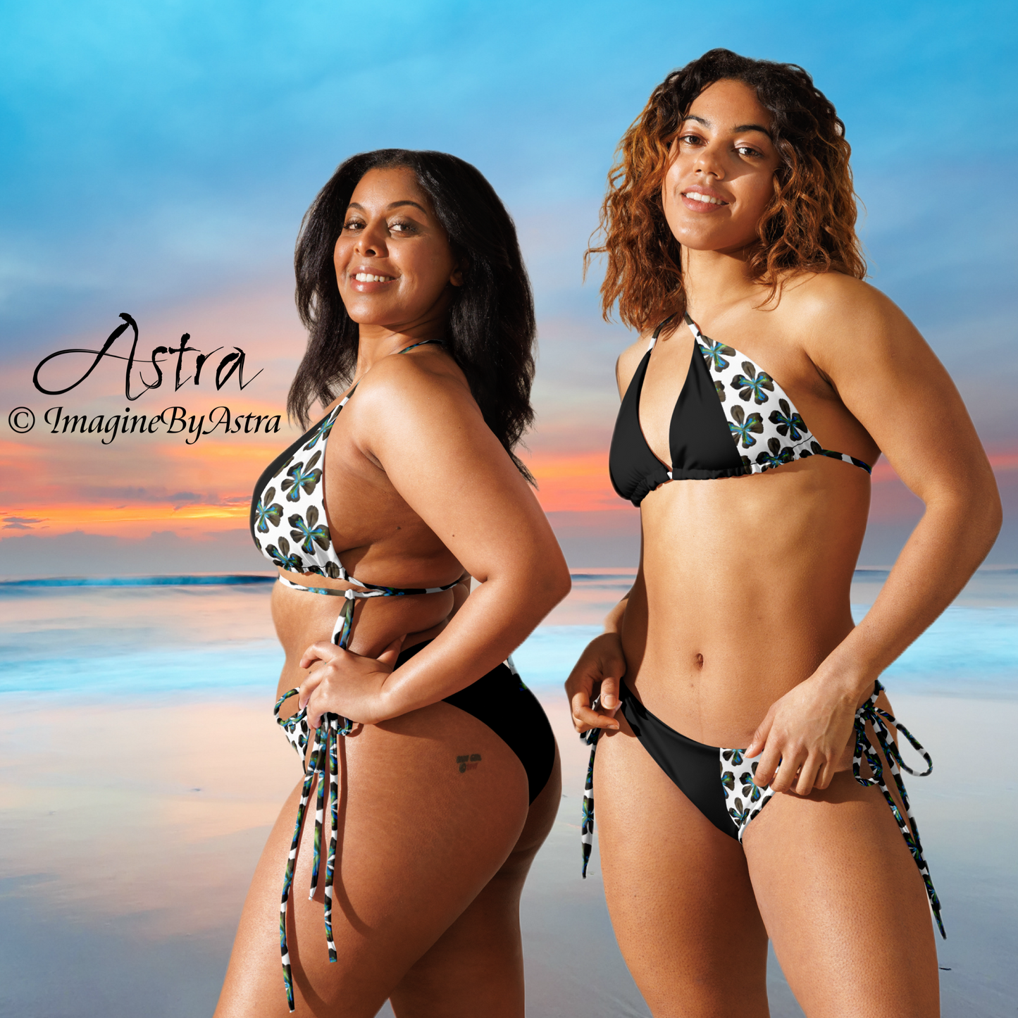 Two black women wear black and white string bikinis with white paneling running down one side with a tropical flower print, a beautiful beach sunset displayed in the background. Part of the Tropical Iris Collection by designer, Imagine By Astra. From the Astra Swimwear lineup.