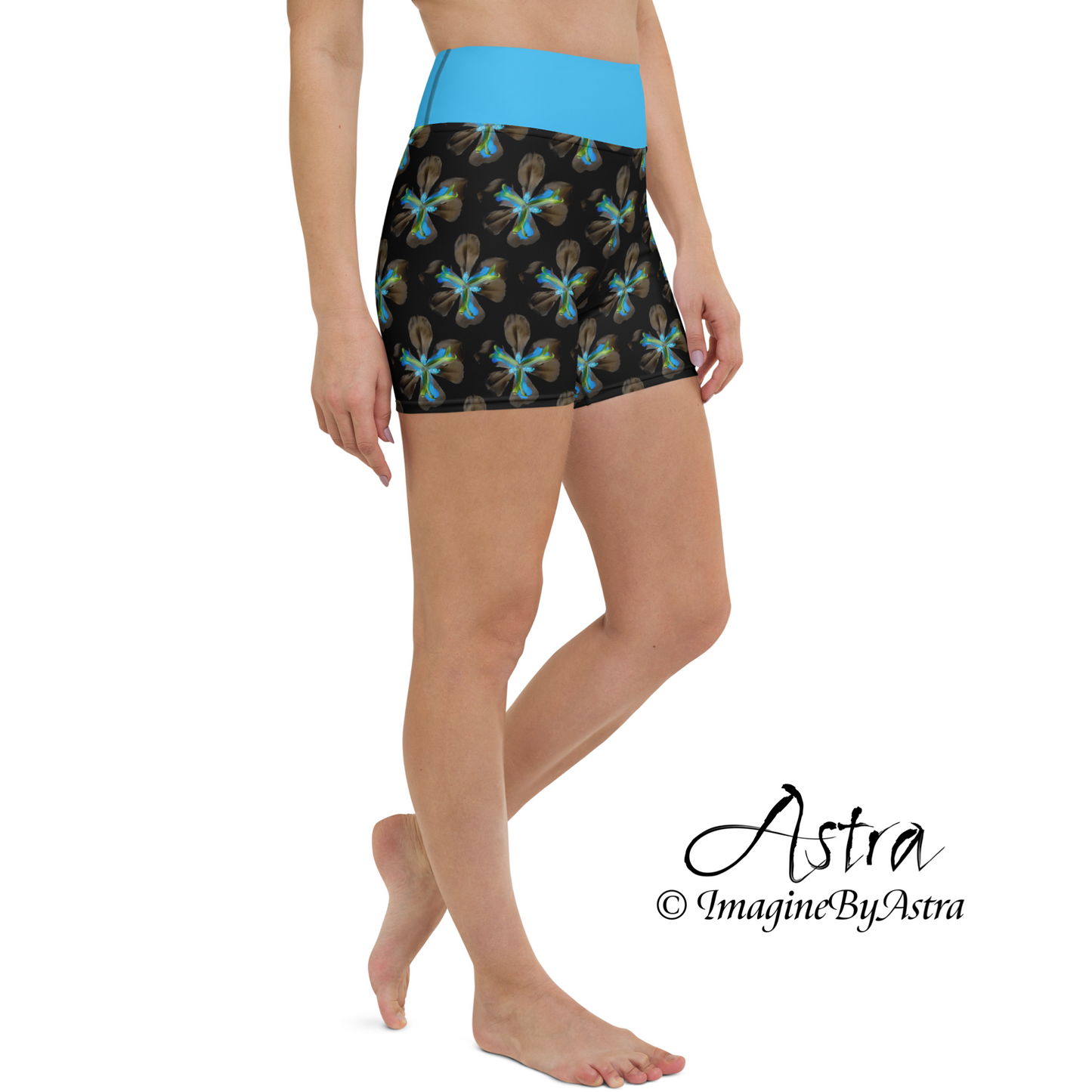 Side view of a white woman wearing a pair of black high-waisted gym shorts with a brilliant blue floral print with matching blue waistband from the tropical Iris Collection from activewear brand, Imagine by Astra.