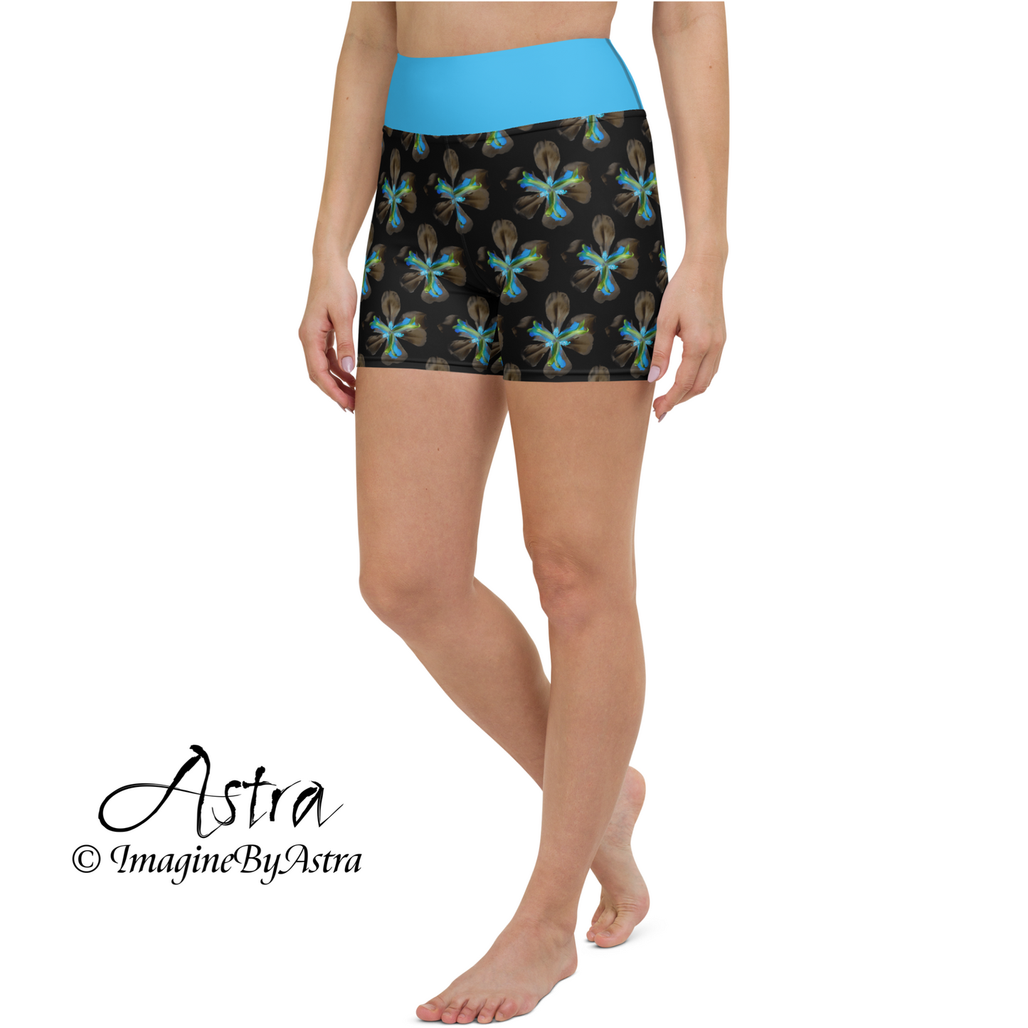 Side view of a white woman wearing a pair of black high-waisted yoga shorts with a brilliant blue floral print with matching blue waistband from the tropical Iris Collection from designer, Imagine by Astra.