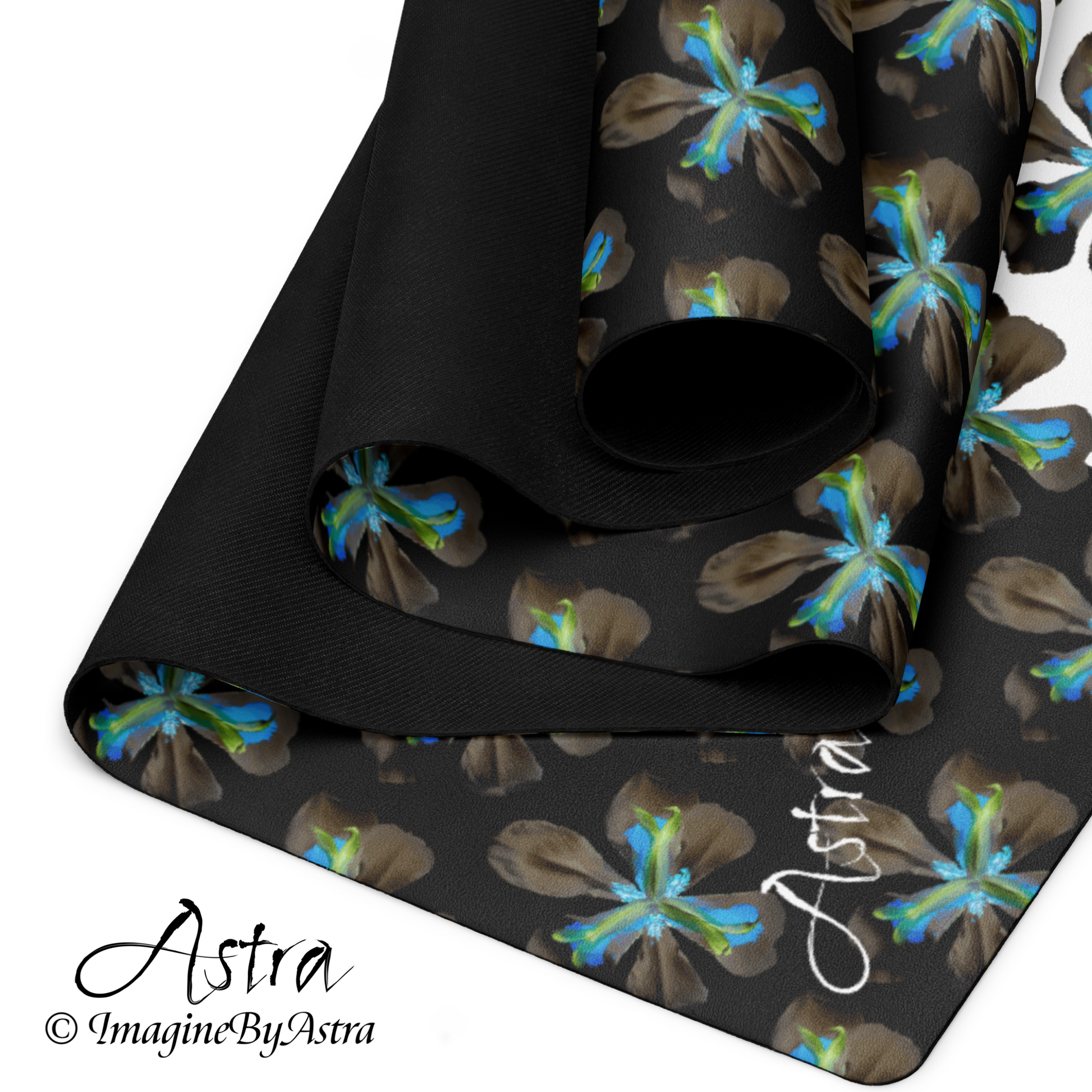 A yoga mat is partially folded back on itself revealing a dramatic two toned black and white surface with a bright blue tropical flower print on top, the black non slip rubber back can be seen on the back of the mat. From activewear brand, ImagineByAstra.