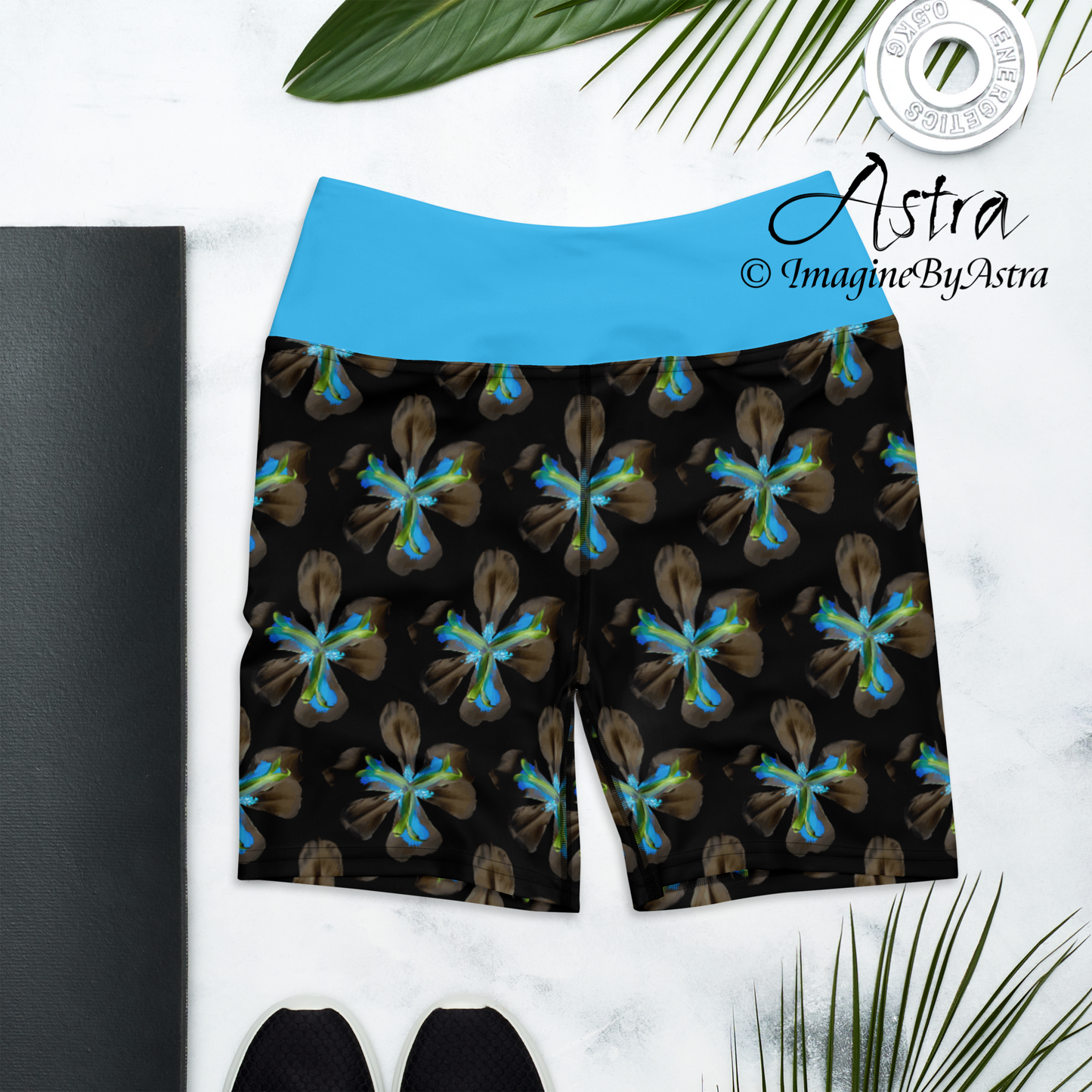 The front of a pair of black high-waisted yoga leggings shorts with a bright blue floral print with matching blue waistband from the Tropical Iris Collection from activewear brand, Imagine by Astra.