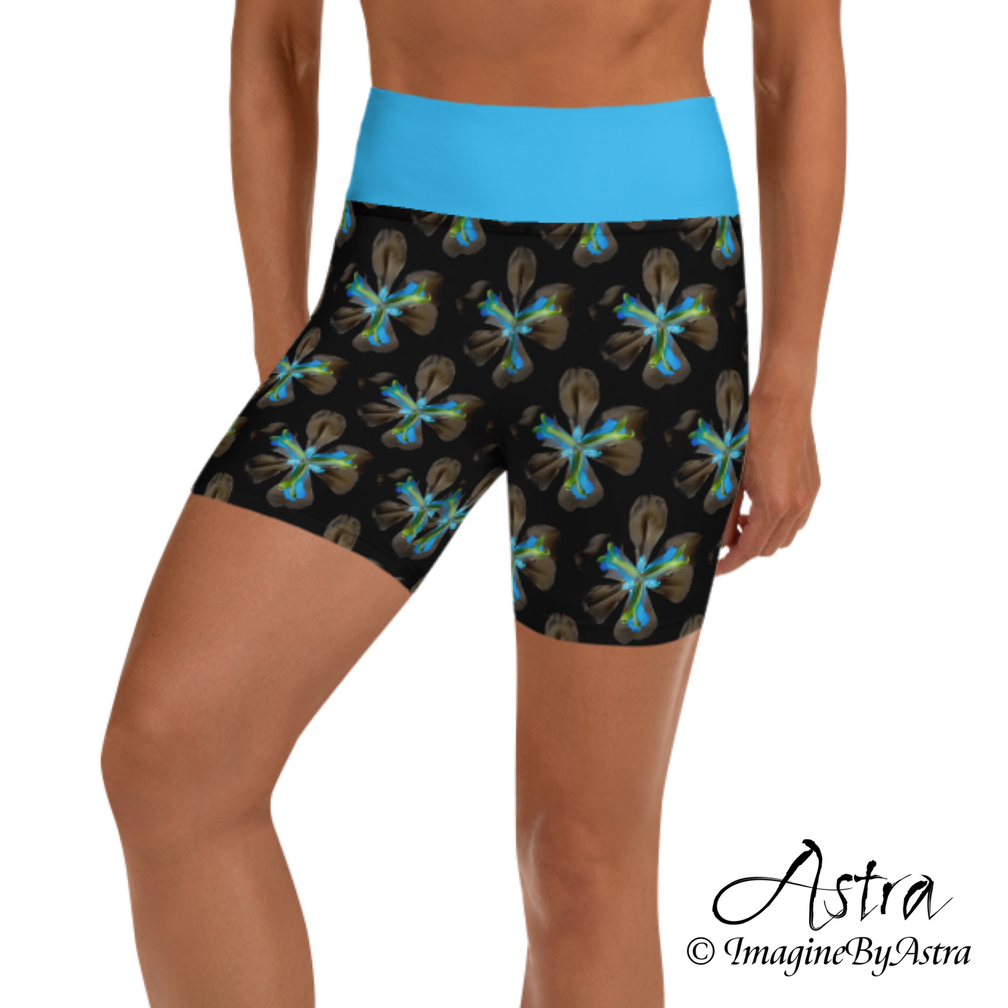 Front view of a white woman wearing a pair of black high-waisted yoga shorts with a brilliant blue floral print with matching blue waistband from the tropical Iris Collection from designer, Imagine by Astra.