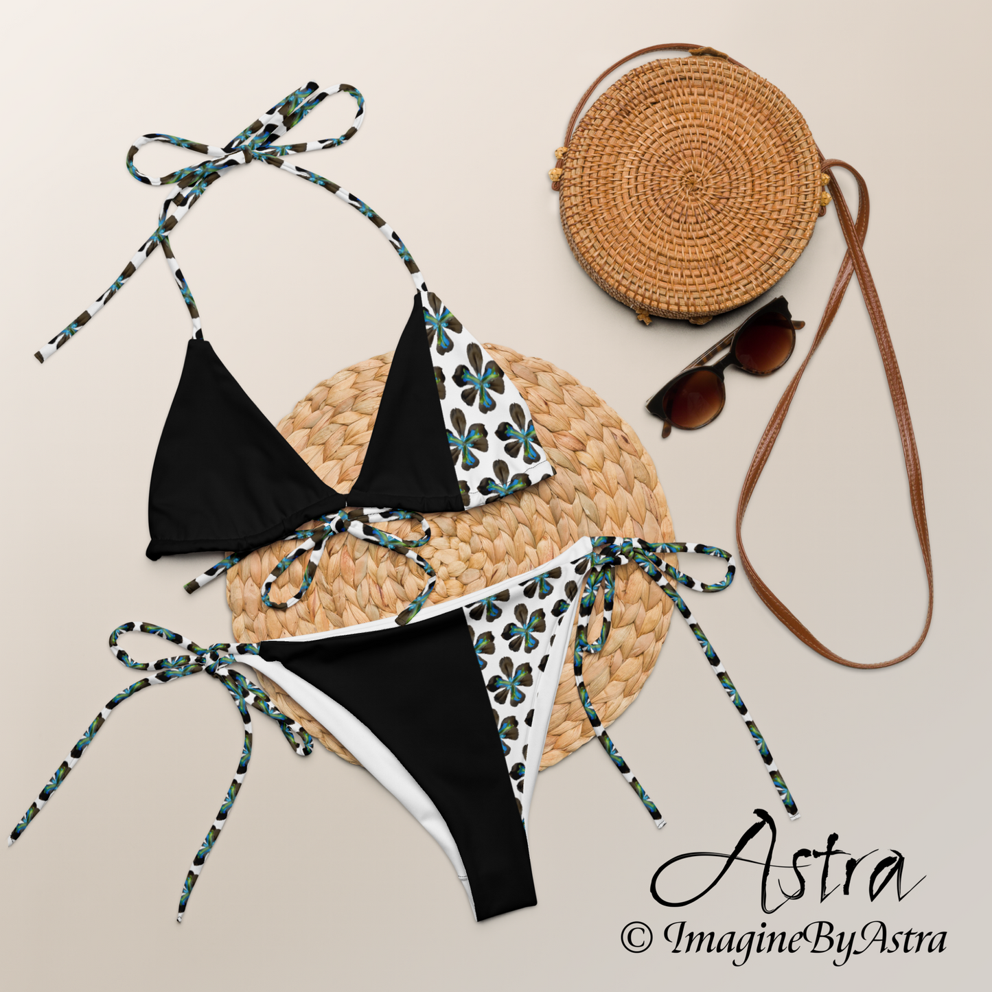 Laid out is a black string bikini with a white panel running down one side with blue tropical flower print, part of the Tropical Iris Collection by designer, Imagine By Astra. Part of the Astra Swimwear lineup.