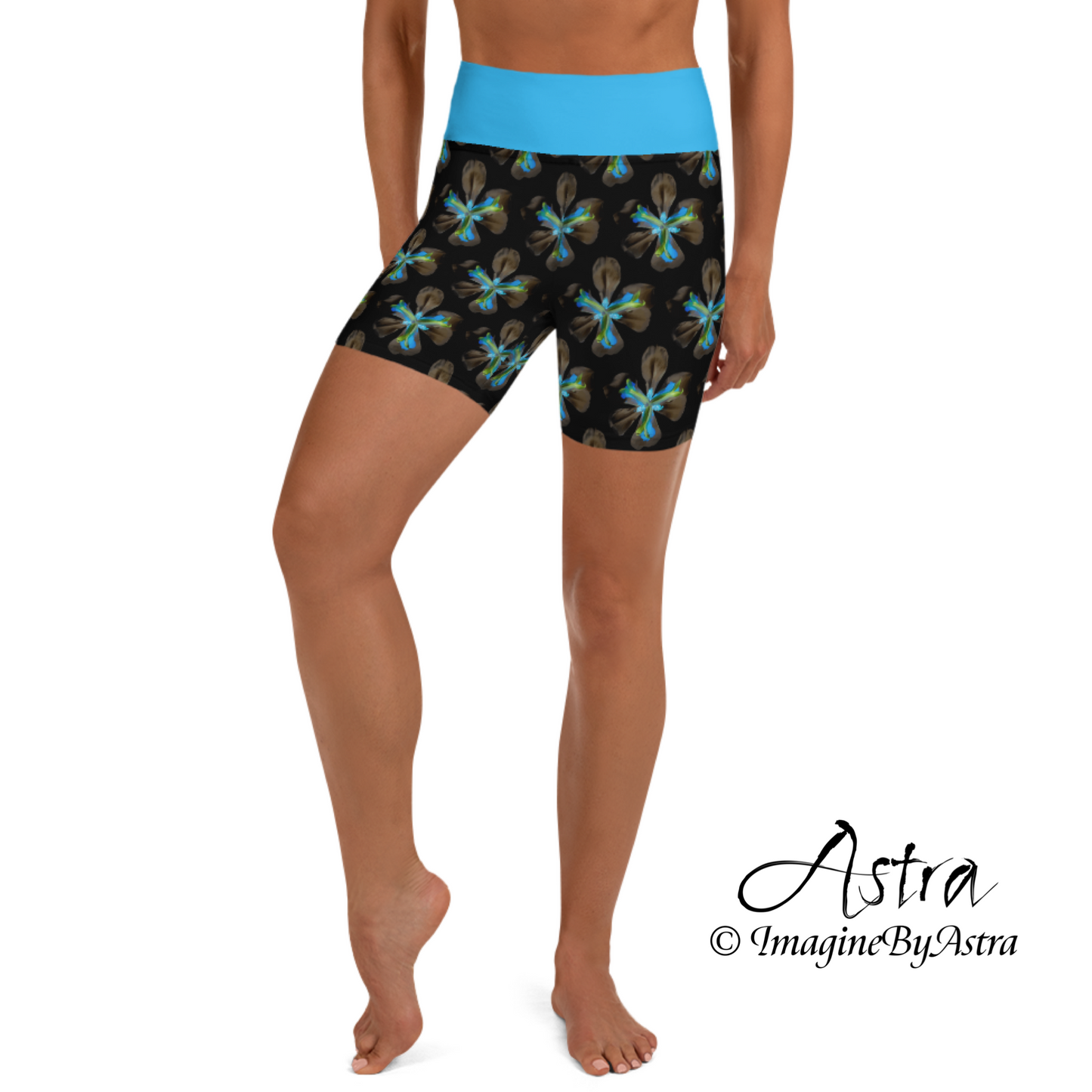 Front view of a white woman wearing a pair of black high-waisted yoga shorts with a brilliant blue floral print with matching blue waistband from the tropical Iris Collection from designer, ImagineByAstra.