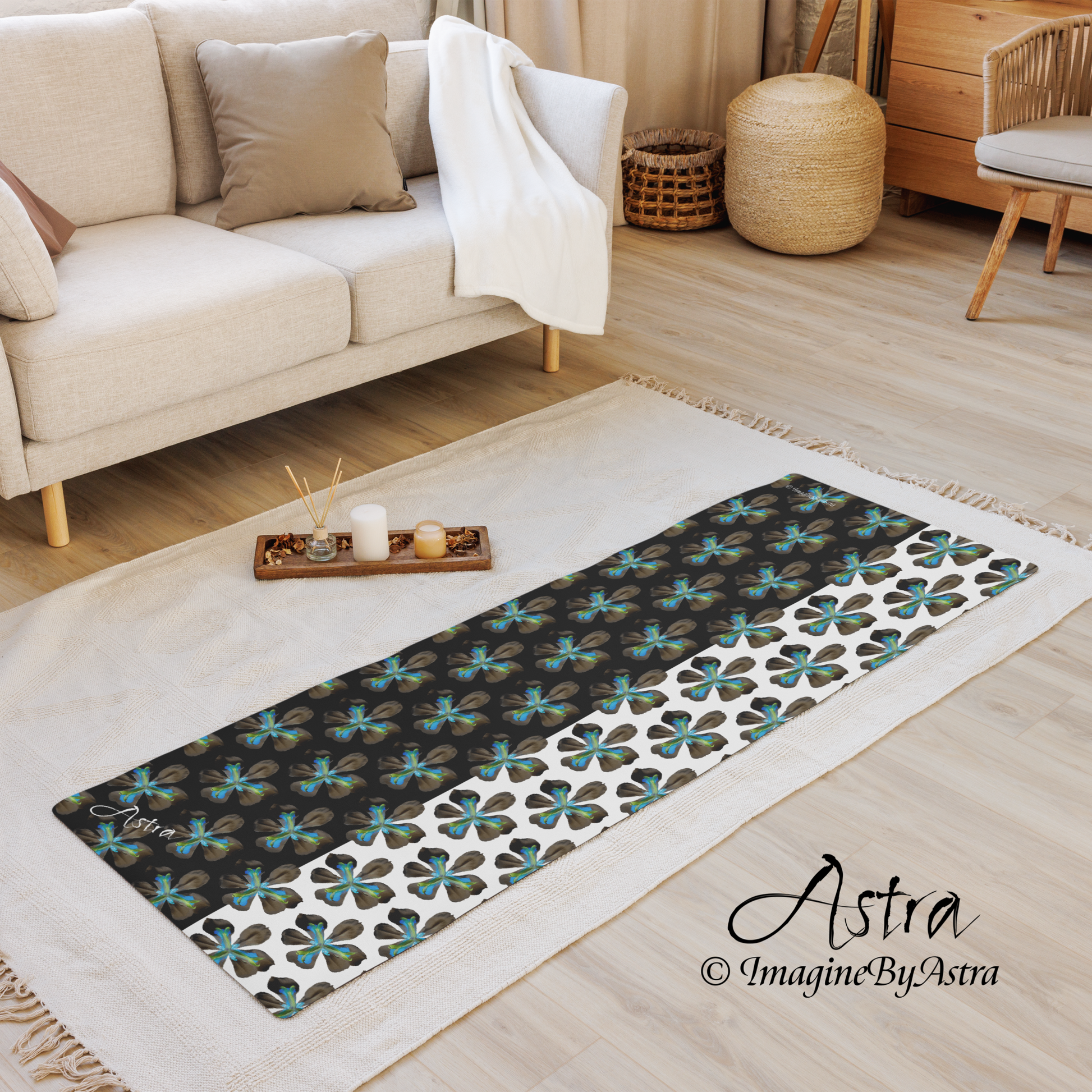 A yoga mat is laid out on a living room rug. It bears a dramatic two toned black and white surface with a bright blue tropical flower print on top. From brand, Imagine by Astra Activewear.