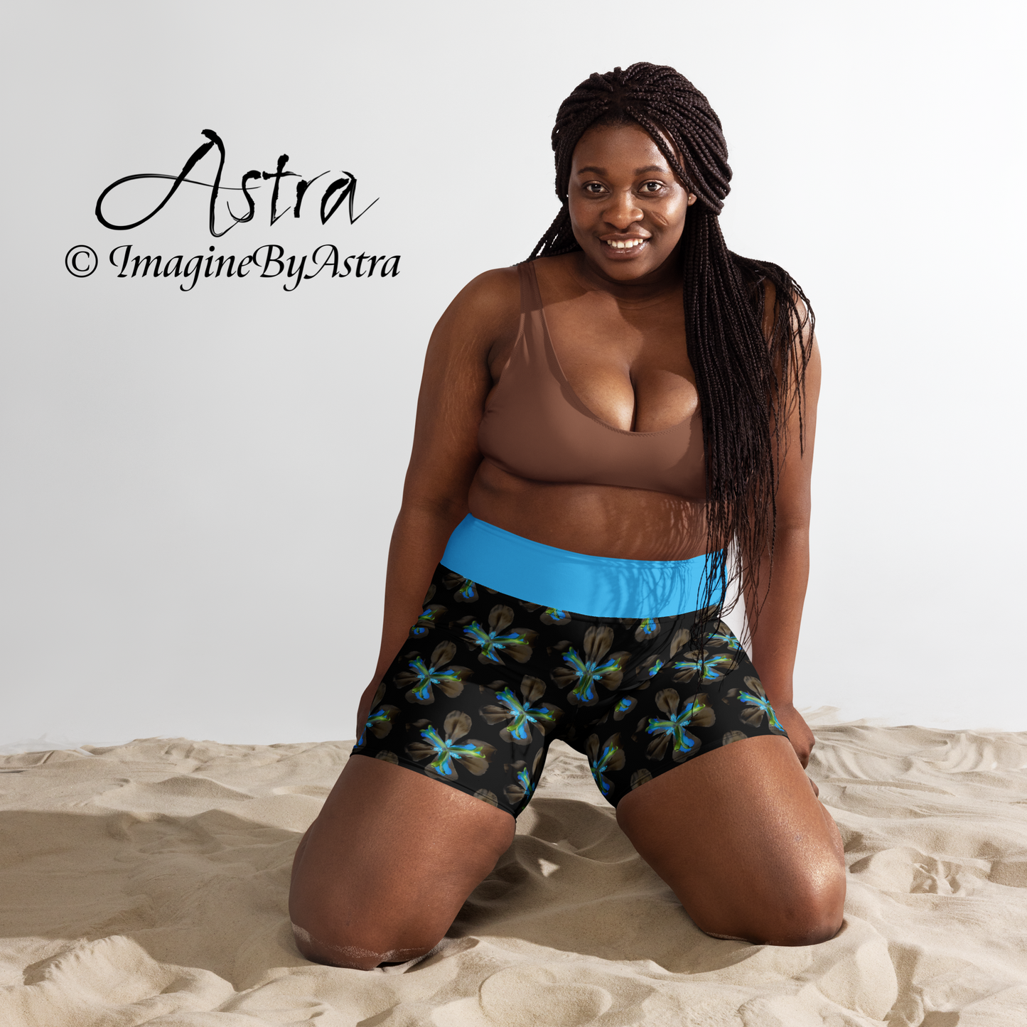 Front view of a black plus size woman wearing a pair of black high-waisted yoga shorts with a brilliant blue tropical floral print with matching blue waistband from the Tropical Iris Collection from designer, ImagineByAstra.