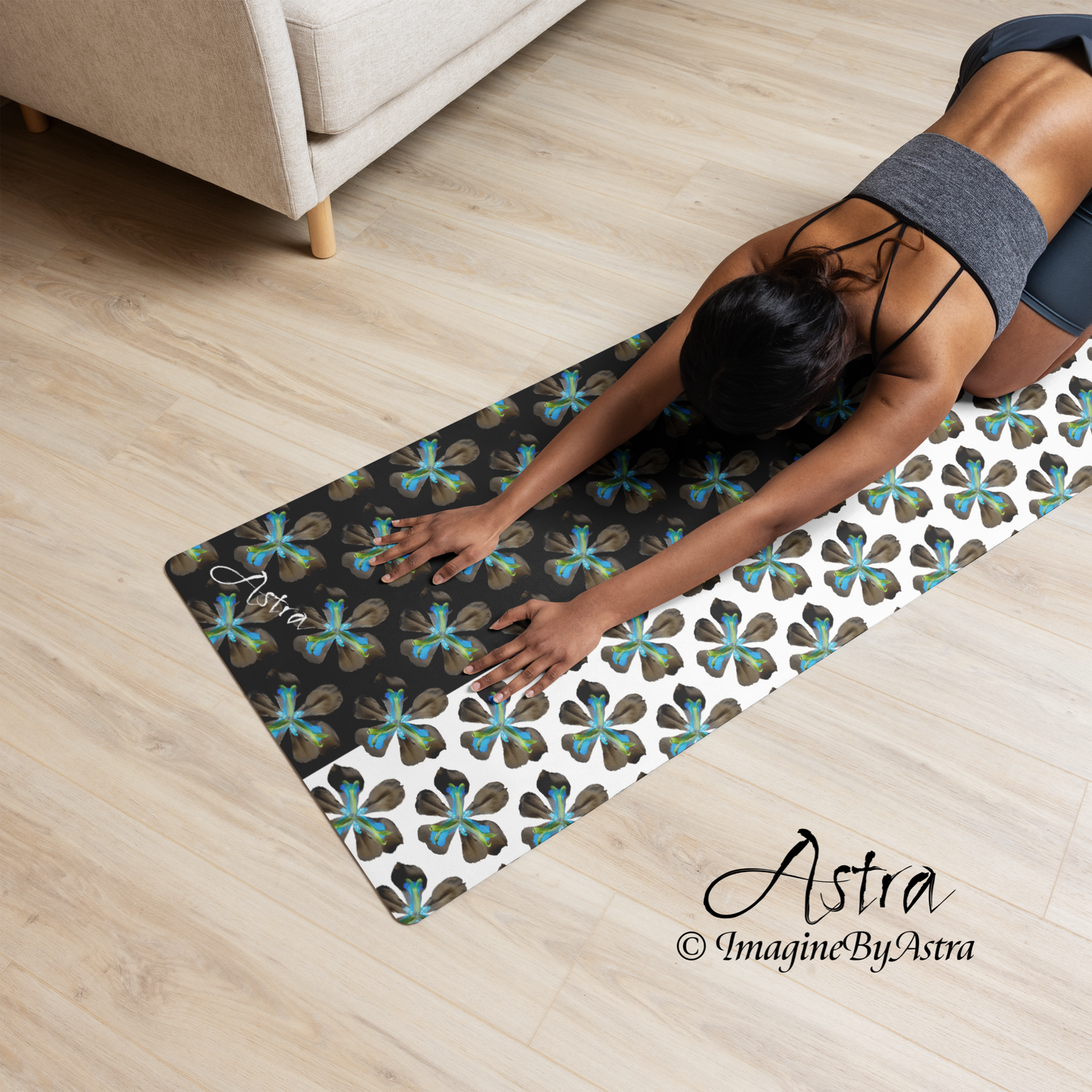 A black woman stretches on a black and white yoga mat with a bright blue tropical flower print from activewear brand, Astra activewear.