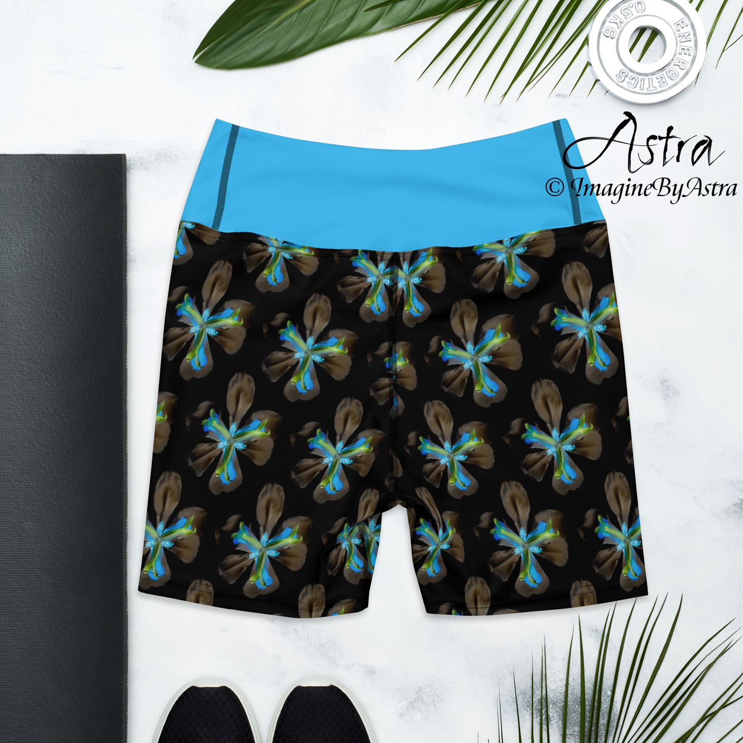 The back of a pair of black high-waisted yoga leggings shorts with a bright blue floral print with matching blue waistband from the Tropical Iris Collection from activewear brand, Imagine by Astra.