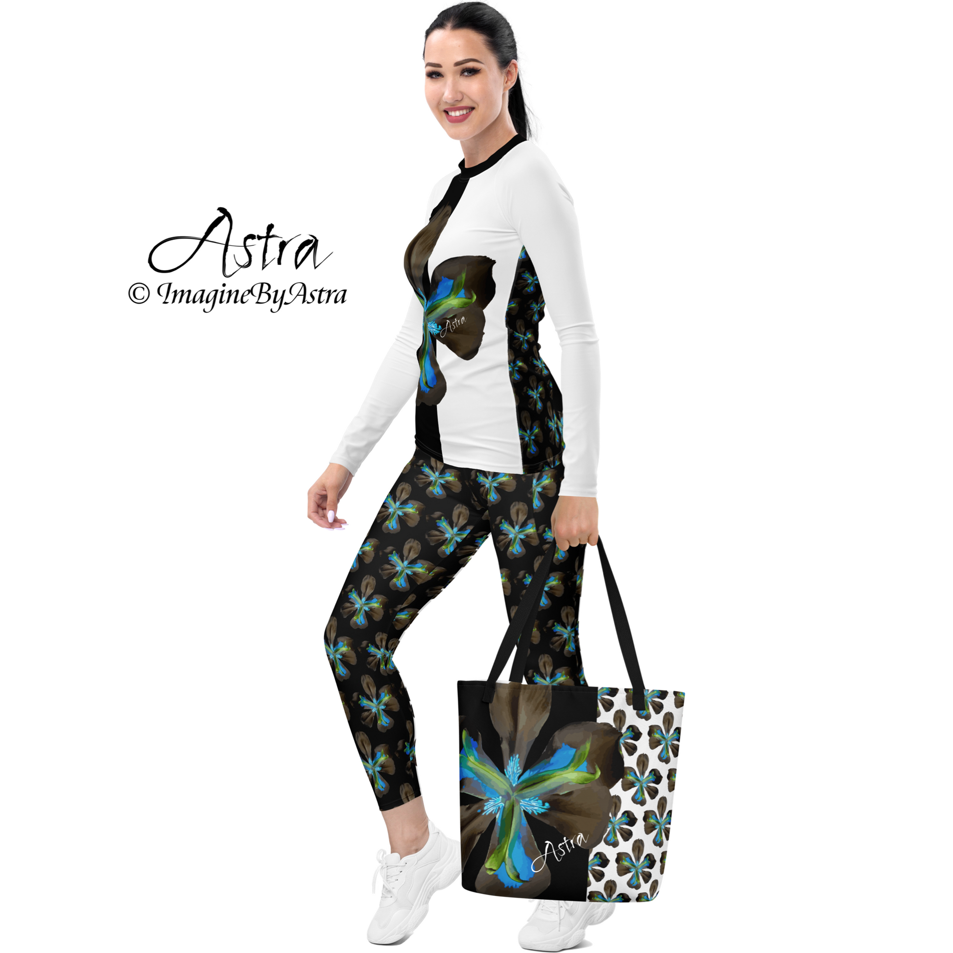 A side view shows a light skinned woman wearing the Tropical Iris Eco-Friendly Leggings in black featuring the electric blue iris flower print. She also wears the matching long sleeved top in white bearing the iris in a single large striking graphic on the front. She is carrying the Astra Tote which features the same bold iris print. Together it is a stunning cohesive ensemble from the Tropical Iris Resort Collection by Imagine by Astra.